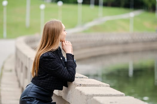 Young woman leans against the railing and looks thoughtfully at the river