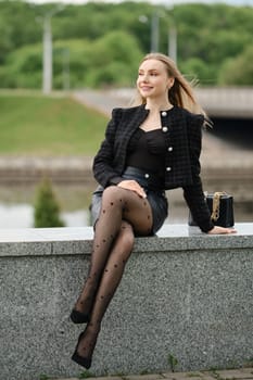 Pretty young woman sitting on river bank in city park near her office