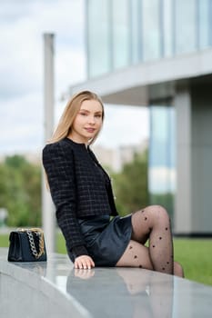 Pretty young woman sitting on marble railing near office building