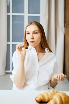 Young woman in white shirt chewing sweet cherry in the kitchen