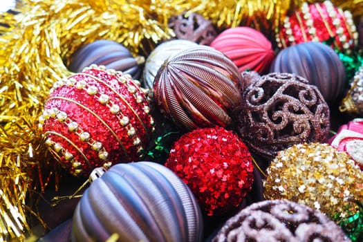 Christmas background with yellow tinsel and Christmas balls. Beautiful Christmas toys and decorations. Red, gold, brown, silver, yellow striped shiny balls. Toy festive train locomotive
