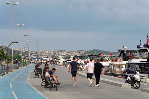 Istanbul, Turkey - August 31, 2022: Pedestrians walking on side walk by the Bosphorus Strait between Bebek and Hisari districts, beside docked boats and yachts, against clear sky on summer day
