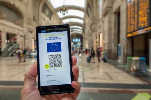 Woman showing on smartphone EU Digital Covid Certificate with quad code. Train station background.