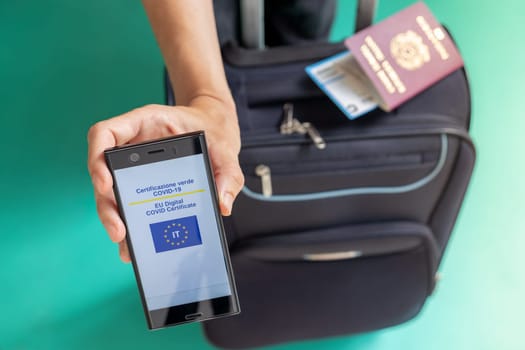 Woman showing on smartphone Italian EU Digital Covid Certificate with quad code. Passport, boarding pass and baggage.