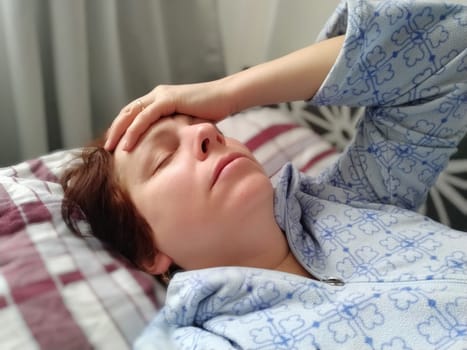 Sick woman in bed. Headache, runny nose and cold. Paleness of the face and faintness of the body. Feeling unwell. The patient holds his forehead with his hand and covers his eyes.