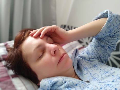 Sick woman in bed. Headache, runny nose and cold. Paleness of the face and faintness of the body. Feeling unwell. The patient holds his forehead with his hand and covers his eyes.