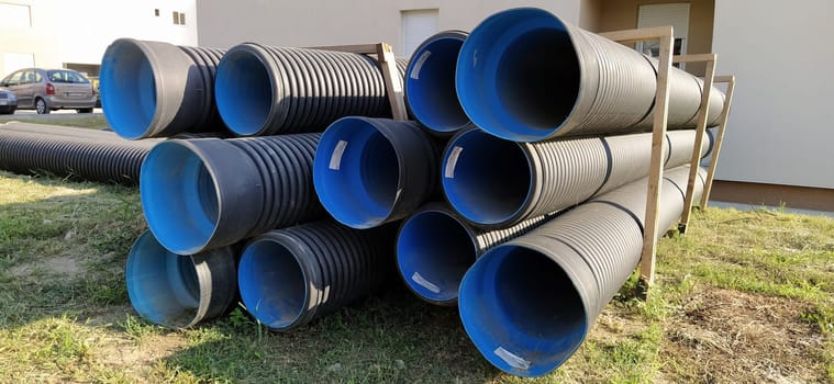 Sremska Mitrovica, Serbia, 23 August 2020. Metal corrugated pipes, blue inside. Plumbing or heating pipes lie on the ground next to a residential building. Corrugated metal.