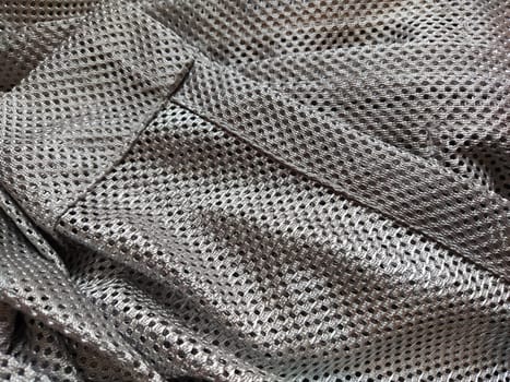 Synthetic polyester fabric with holes. Abstract background. A wave-folded piece of fabric in gray or silver color. Neatly hemmed fabric