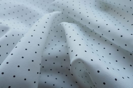 Texture of silk fabric. Black polka dots on a white background. Dress lightweight synthetic fabric in white with a repeating pattern. The textile is made up of waves and folds. Feminine classic style