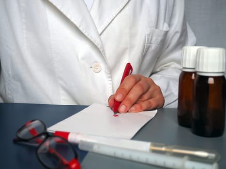 A left-handed doctor is writing something down on paper. Pen for writing in hand. A white coat is worn by a medical professional. Hands of a doctor or nurse. Medicines, glasses, test tubes
