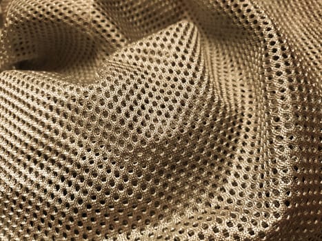 Synthetic polyester fabric with holes. Abstract background. A piece of fabric, folded in waves, in yellow or gold. Furniture upholstery.