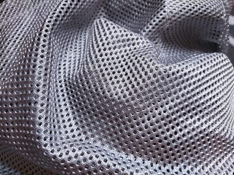 Synthetic polyester fabric with holes. Abstract background. A wave-folded piece of fabric in gray or silver color