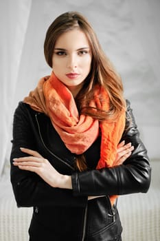 Trendy woman in leather jacket and silk scarf over her neck standing with crossed arms
