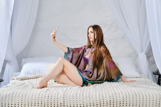 Calm satisfied woman relaxing on comfortable bed enjoying weekend at home and making online video call