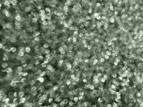 Bokeh light of white glitters. Black grey white silver glitter texture background. Sparkling glitter wrapping paper with sequins and sparkles. Festive bokeh and glitter. Green tint.