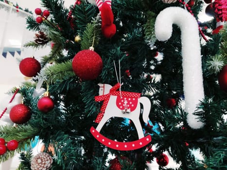 Christmas tree with decorations, Christmas balls and toys. Red and white hanging ornaments. Beautiful balls, bright berries and cones. Snow candy stick. Toy - rocking horse.