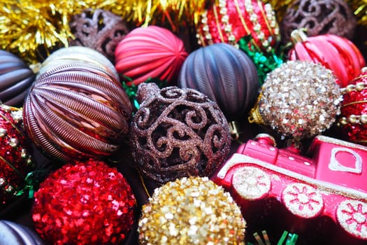 Christmas background with yellow tinsel and Christmas balls. Beautiful Christmas toys and decorations. Red, gold, brown, silver, yellow striped shiny balls. Toy festive train locomotive