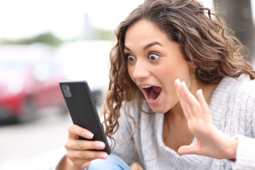 Surprised woman checking smart phone content in the street