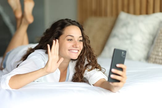 Happy woman in a video call on phone on the bed in the bedroom