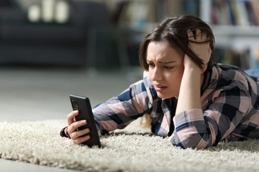 Sad teen checking smart phone on the floor at home in the night
