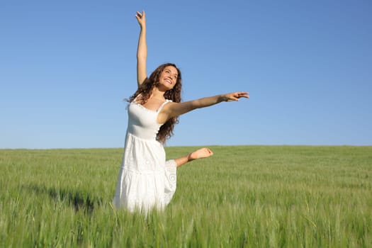 Happy woman with white dress dancing in a green wheat field