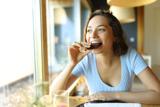 Happy woman eating chocolate cake sitting in a restaurant