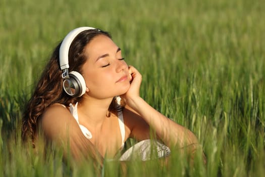 Woman relaxing listening to music wearing headphones in a green barley field