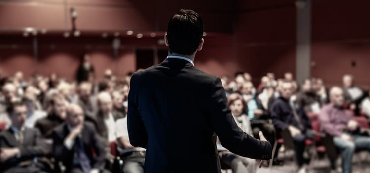 Speaker giving a talk on corporate business conference. Unrecognizable people in audience at conference hall. Business and Entrepreneurship event.