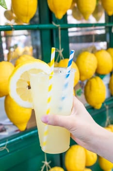 Caucasian hand with healthy fresh lemonade during summer with lemons background
