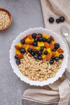 Oatmeal porridge with blueberries, mango and almonds in bowl on concrete grey table from above. flatlay. Healthy breakfast food. Copy space