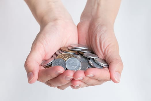 A woman's hands cupped holding many various Japanese Yen coins with a white background.