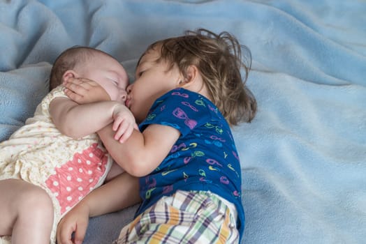 A 2 year old boy and his newborn sister lying on a bed.