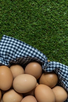Basket contains group of chicken eggs put on grass.