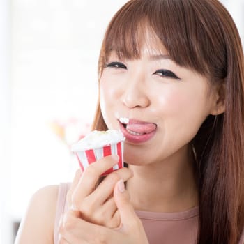 Portrait of attractive Asian girl eating cupcake and licking on her lips. Young woman indoors living lifestyle at home.
