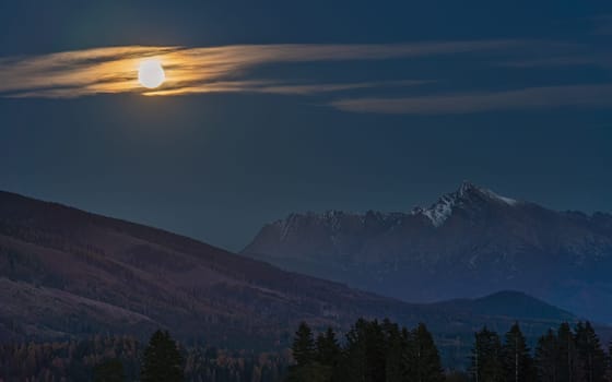 Full moon over mount Krivan peak - Slovak symbol - forest trees silhouettes in foreground, evening photo.