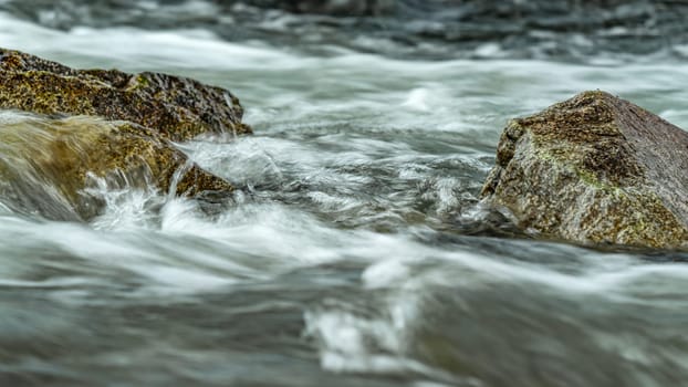 Rapid spring river flowing over rocks forming white water waves, closeup detail - abstract nature background.