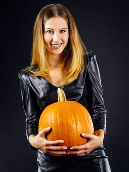 Young sexy woman in leather holding a pumpkin over smoky dark background for Halloween.