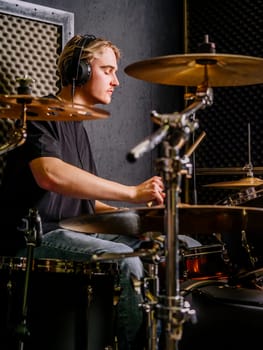Young man wearing headphones and playing drums in a recording studio.