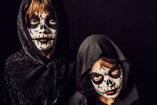 Two kids wearing dark robes and scary face paint at Halloween.