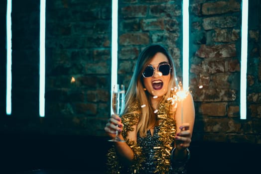 Young happy woman celebrating new year eve drinking champagne with fireworks and confetti. Lady clubber in nightclub having fun. Hipster girl at celebration luxury party.