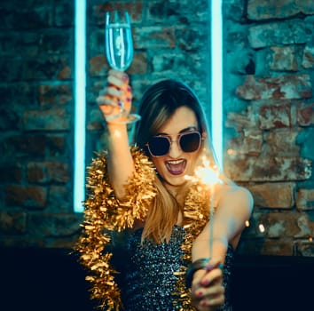 Young happy woman celebrating new year eve drinking champagne with fireworks. Lady clubber in nightclub having fun. Hipster girl at celebration luxury party.
