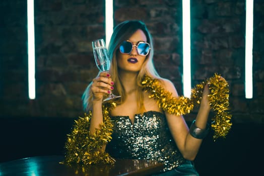 Young happy woman celebrating new year eve drinking champagne. Night lights and confetti. Lady clubber in nightclub having fun. Hipster girl at celebration luxury party.