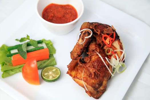 Big cut of delicious asian fried chicken with chili sauce sambal and vegetables on white plate background