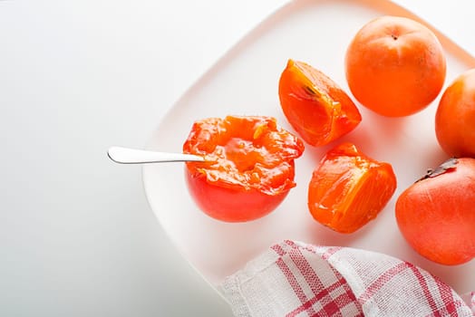 Ripe red and yellow orange persimmon fruit. Slices of persimmon. Close up of fresh kaki on white table
