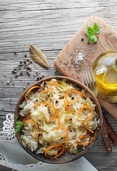 Homemade sauerkraut with carrot, black pepper and parsley in bowl on rustic background. Top view. Copy space