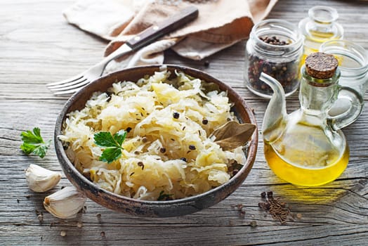 Homemade sauerkraut with black pepper and parsley in bowl on rustic background.