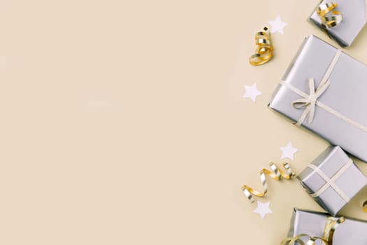 Light beige or yellow flat lay background with gift boxes in glossy silver craft paper packaging with golden ribbon and stars. Copy space for Valentine's Day, Mother's Day, Birthday or Christmas