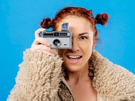Beautiful redhead holding a vintage 35mm camera with cube flash over blue background.