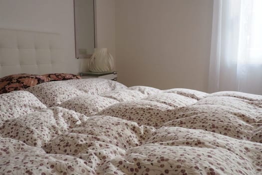 Double bridal bed with pillows and thick feather duvet. Bedroom design. Soft white headboard. Interior with furniture and bedding