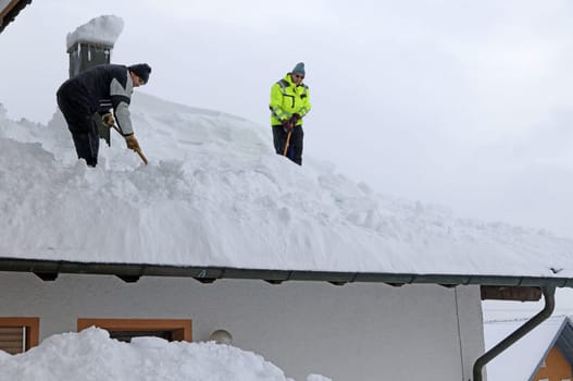 Two men shoveling high heavy snow from a house roof